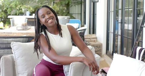 Smiling young woman relaxing on outdoor patio armchair, casual modern porch lifestyle