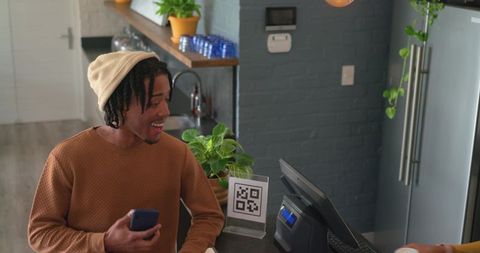 Urban cafe customer scanning qr code for contactless payment with smartphone at counter