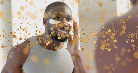 Smiling man applying under-eye patches at mirror during morning skincare routine for men