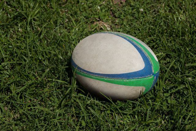 High angle view of a rugby ball resting on a grassy field. Ideal for use in sports-related content, outdoor activity promotions, and recreational event advertisements. Perfect for illustrating rugby games, training sessions, or general sports themes.