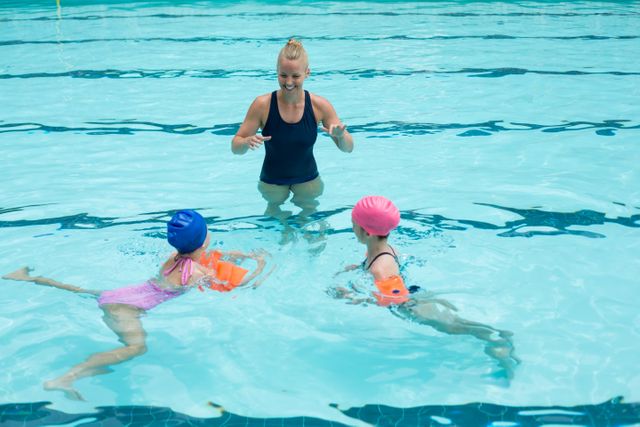 Swimming instructor teaching children in a pool, ideal for use in educational materials, sports training guides, summer camp promotions, and health and fitness content. Highlights the importance of water safety and learning to swim at a young age.