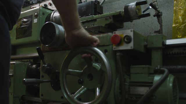 Close up of a Caucasian male factory worker at a factory, wearing dark blue t shirt, operating the machine, in slow motion.