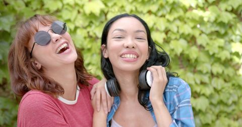 Two Young Women Laughing Outdoors with Headphones and Sunglasses