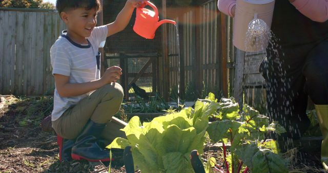 Senior biracial grandmother and grandson watering plants in sunny garden. Family, togetherness, nature, gardening and lifestyle, unaltered.