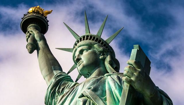 Epic close-up of statue of liberty torch and crown with patina detail against blue sky