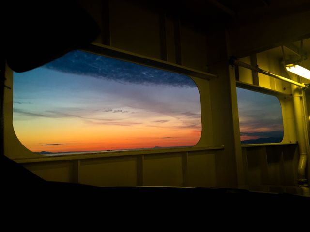 Sunset view framed through the window of a ferry, capturing the vibrant evening sky with orange and blue hues. Ideal for use in travel blogs, nautical-themed content, or promotional materials for ferry services.