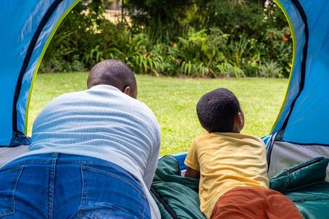 African american father and son lying in tent looking out at sunny backyard lawn