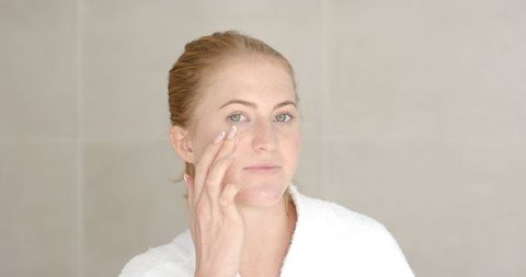 Woman Applying Facial Cream for Self-Care in Minimalistic Bathroom