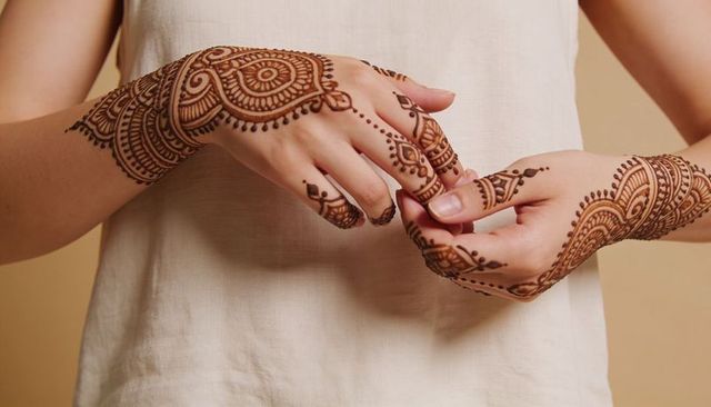 Woman displaying intricate henna on forearms and fingers in cream sleeveless top