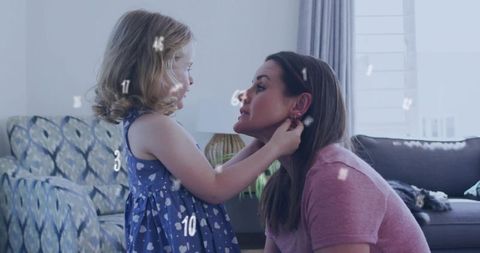 Mother daughter bonding: little girl adjusting mom's earring in warm home interior