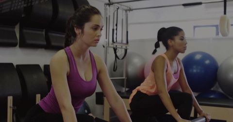 Focused duo pedaling stationary bike cardio workout in bright fitness studio