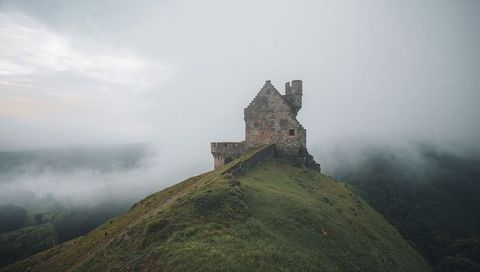 Crumbling stone castle crowning misty ridge, ancient turret overlooking fog-filled valley