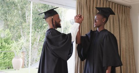 Two Recent Graduate Students Celebrating Achievement at Home in Gowns
