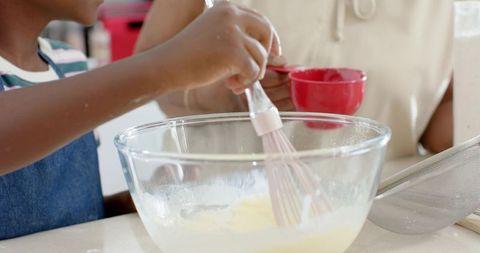 African american senior and youth women stirring batter in glass bowl for home baking