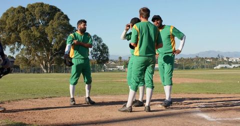 Diverse baseball team huddling at home plate in green and yellow uniforms