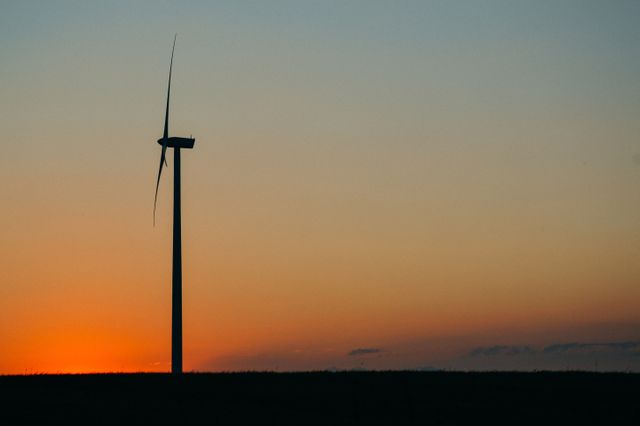 Capture of a solitary wind turbine against a vibrant sunset sky. Ideal for illustrating concepts of renewable energy, sustainability, and the beauty of technology in nature. Suitable for use in environmental campaigns, renewable energy articles, and eco-friendly advertising.