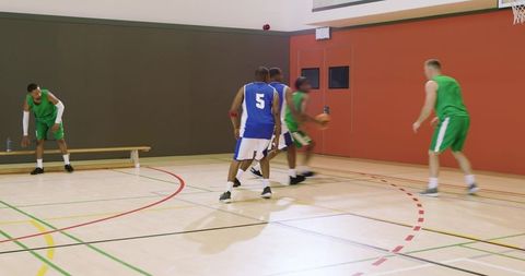 Players colliding and recovering ball, dribbling toward baseline in indoor basketball game