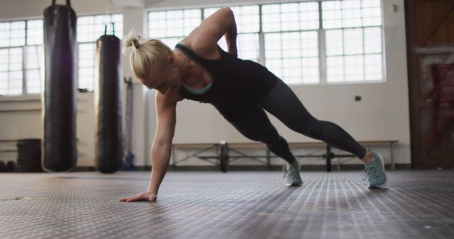 Woman performing one-arm push-up in gym. Demonstrating strength and balance. Ideal for fitness and training advertisements, workout routine illustrations, or sportswear promotions.