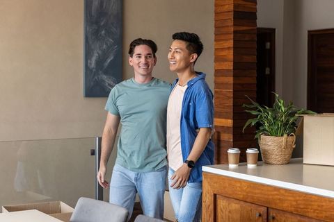 Two men standing and smiling in modern kitchen unpacking boxes and enjoying coffee