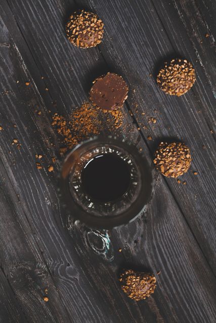 Top view of coffee with chocolate truffles on rustic dark wooden table. Ideal for food blogs, gourmet snack advertisements, decadent dessert promotions, and coffee shop menus highlighting indulgent treats and beverages. Showcases an element of cozy and inviting ambiance.