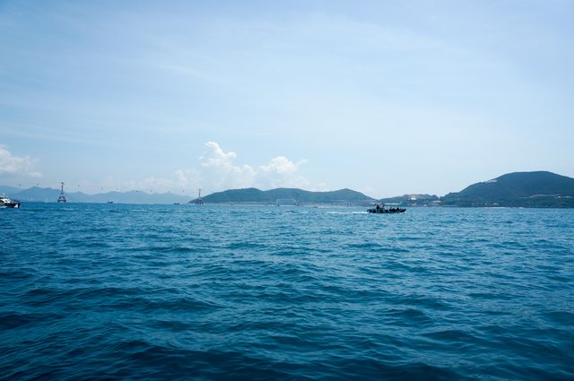 Photograph depicts a tranquil sea with deep blue water, clear skies, and distant mountains. Suitable for articles and websites about travel, nature, outdoor activities, tranquility, or environmental topics. Can be used as a background image for relaxation, wellness or tourism advertising. Perfect for adding text overlay for travel blogs or brochures.