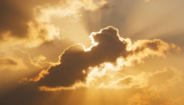 Glowing backlit cumulus cloud at sunrise with golden sunbeams radiating through sky