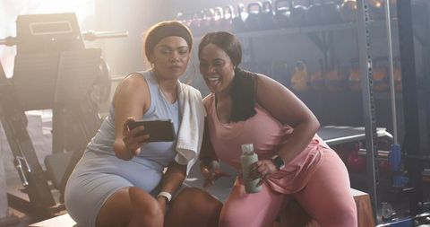 Diverse women checking smartphone after gym workout while laughing in activewear