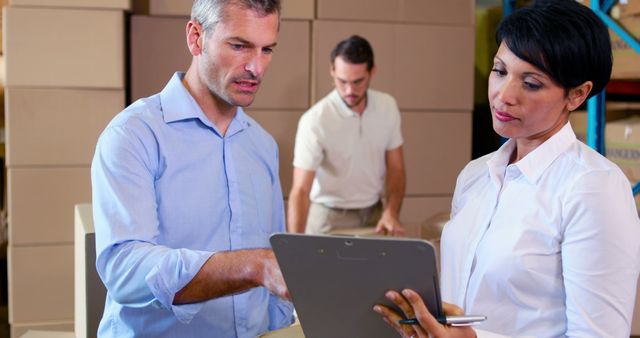 Managers in a warehouse converse while a worker in the background sorts packages. An image suitable for illustrating teamwork, logistics management, or efficient warehouse operations. Ideal for use in business, supply chain, and team collaboration-related projects.