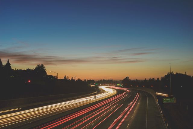 Captures busy highway with light trails at dusk. Sky transitions from orange to deep blue. Suitable for depicting themes of travel, speed, and urban scenics. Ideal for transportation marketing, evening cityscapes, and energy-focus projects.