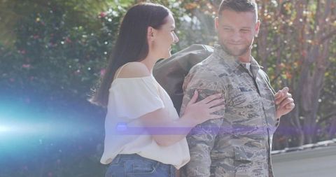 Smiling servicemember returning home embracing partner in sunlit yard with duffel