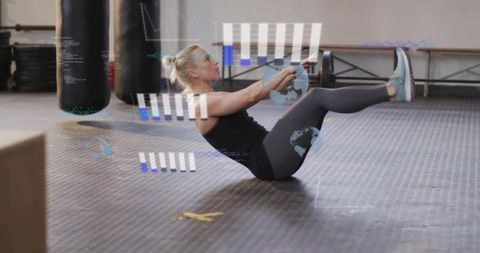 Female Athlete Holding V-Sit Core Exercise Balancing on Gym Floor with Punching Bags
