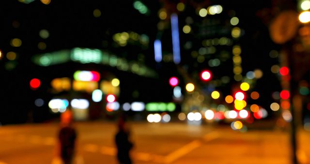 Blurred yet colorful city lights providing vibrant backdrop at night. Highlights bustling atmosphere and nightlife of urban area with traffic lights and people silhouettes. Perfect for portraying themes of urban life, nightlife, cityscapes, modern living, and dynamic environments.