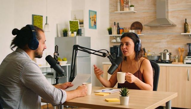 Co-hosts recording conversational podcast at home kitchen table with microphones