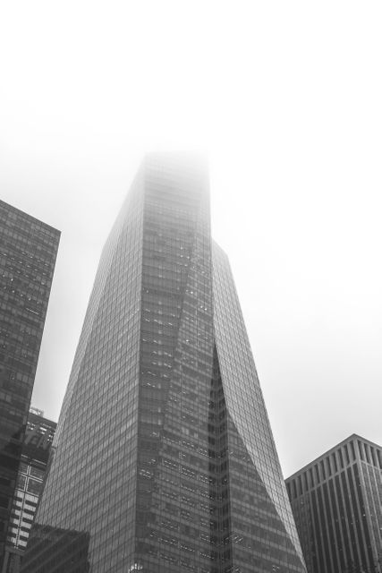 Tall urban skyscrapers enveloped in fog, highlighting the sleek and modern architecture of a cityscape. Appropiate for concepts such as urbanization, business, finance, and modern architecture. Ideal for marketing materials, business presentations, and publications touching on urban development and city living.