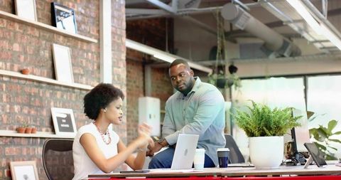 Collaborating coworkers discussing project at industrial office desk with laptop and plants