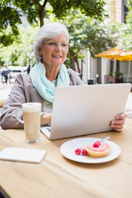 Smiling senior woman using laptop in outdoor cafÃ©