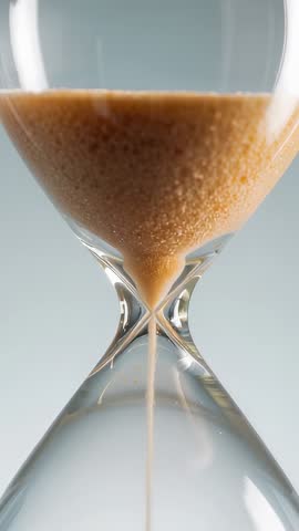 Close-up vertical video showing hourglass pouring amber sand in slow motion, time flowing