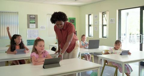 African American teacher guiding elementary students with tablets in modern classroom