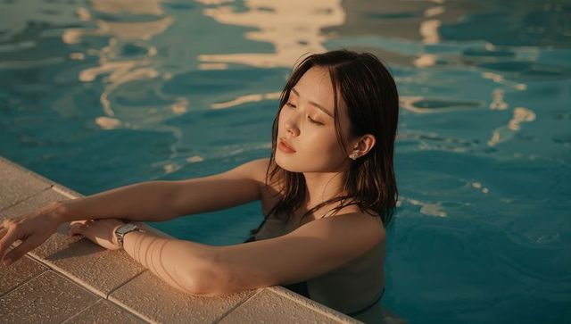 Sunlit poolside contemplation: woman resting on tiled edge during golden hour