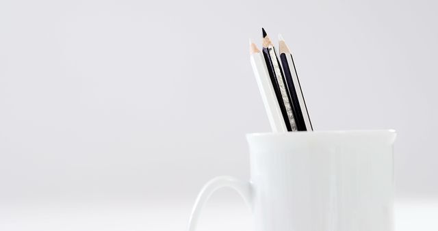 Pencils of varying lengths are arranged in a white mug, with copy space. This minimalist setup suggests a work or study environment, emphasizing organization and simplicity.