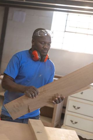 African american carpenter inspecting wooden plank at workbench