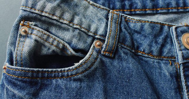 Detailed photo showcasing the texture and stitching of a blue denim jeans pocket with brass rivets. Useful for fashion websites, textile industry, blogs about casual wear, or illustrating articles on denim clothing.