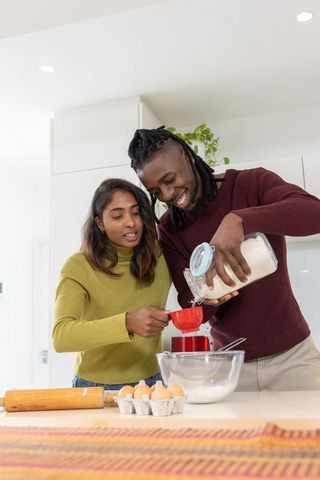 Multiracial couple baking together in modern kitchen measuring sugar and sifting flour