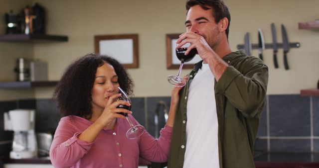 Happy diverse couple standing in kitchen, drinking red wine and embracing. spending free time together at home.