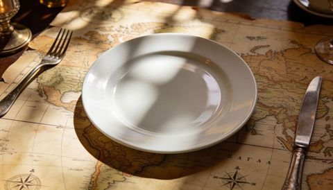 White plate catching dappled sun on vintage world map placemat with silver cutlery