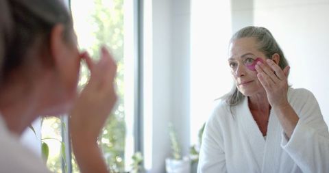 Mature Woman in Bathrobe Applying Skincare in Bright Natural Light