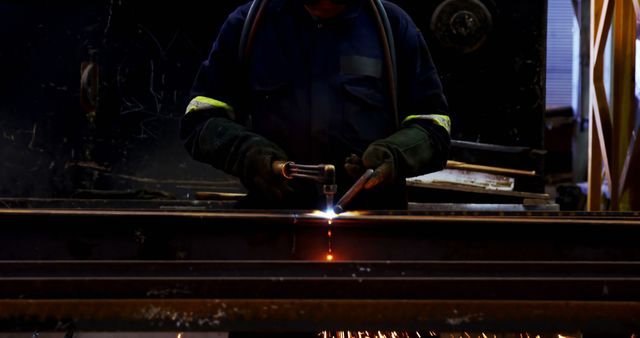 Worker welds metal in a dark industrial environment. Precision and skill are evident as sparks fly from the welding process.