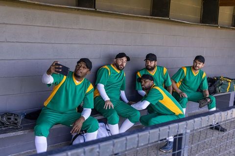 Baseball teammates taking selfie on dugout bench wearing green and yellow uniforms
