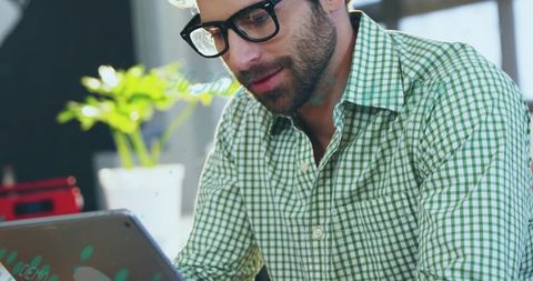 Focused bearded man wearing glasses checking tablet in minimal home workspace