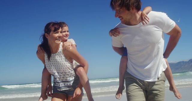 A family of four enjoys a sunny day at the beach. Mother and father carrying their children on piggyback rides while smiling and facing the waves. This image is perfect for illustrating family vacations, beach outings, summer activities, and advertising campaigns geared towards family travel and leisure.